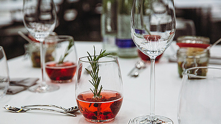 Ein gedeckter Tisch mit einem leeren Weinglas und einem Aperitif im Vordergrund. 