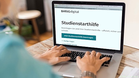 Symbolbild mit Laptop, auf dem die Startseite für die Studienstarthilfe von bafoeg-digital.de.